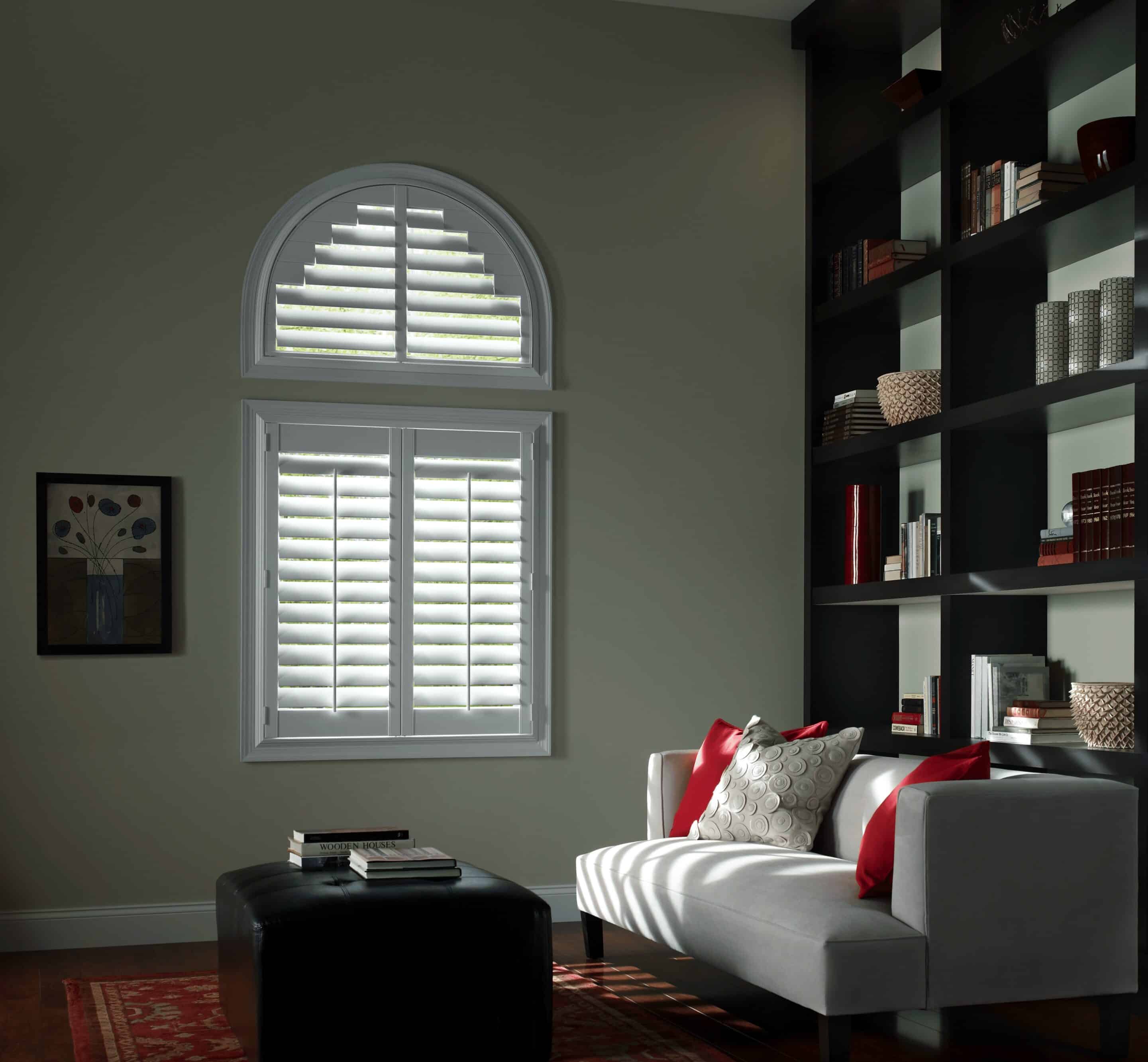 Arched windows with custom made plantation shutters filtering in light into a living room.