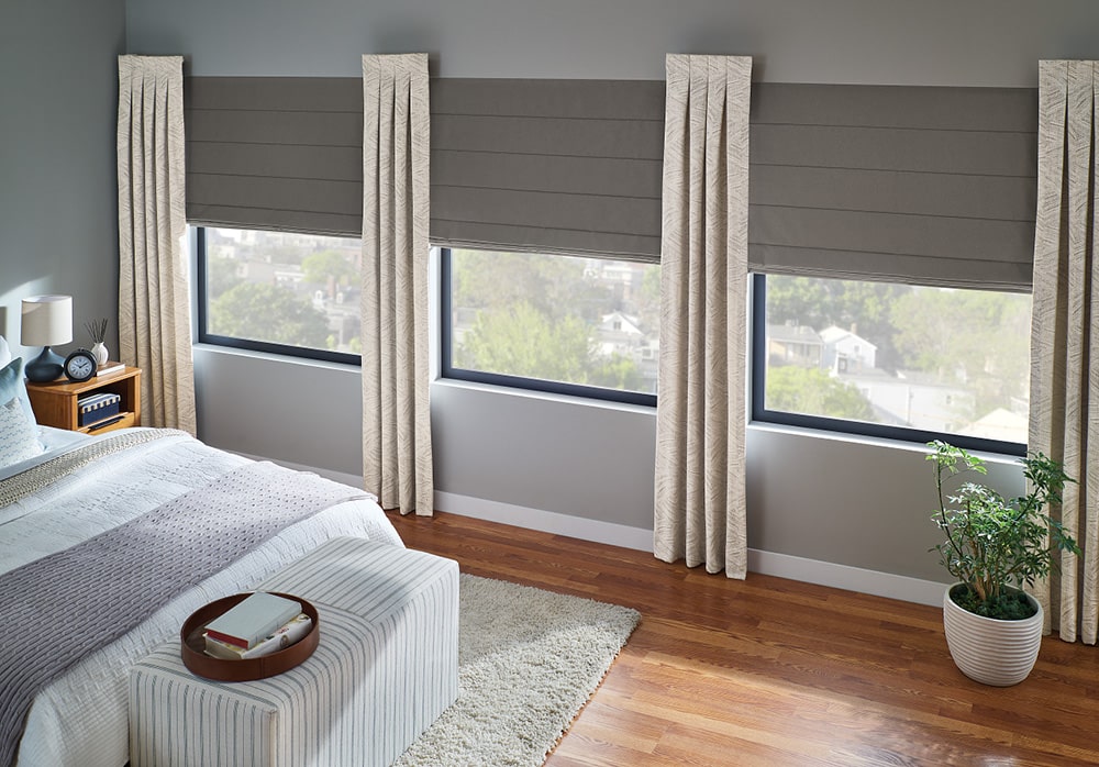 layered drapery and roman shades filtering in light in a master bedroom.