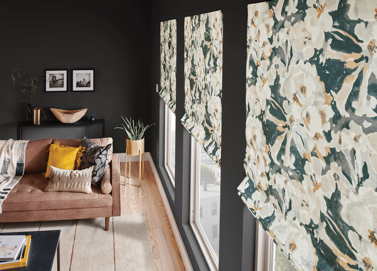 Flower patterned roman shades with light streaming through into a living room.